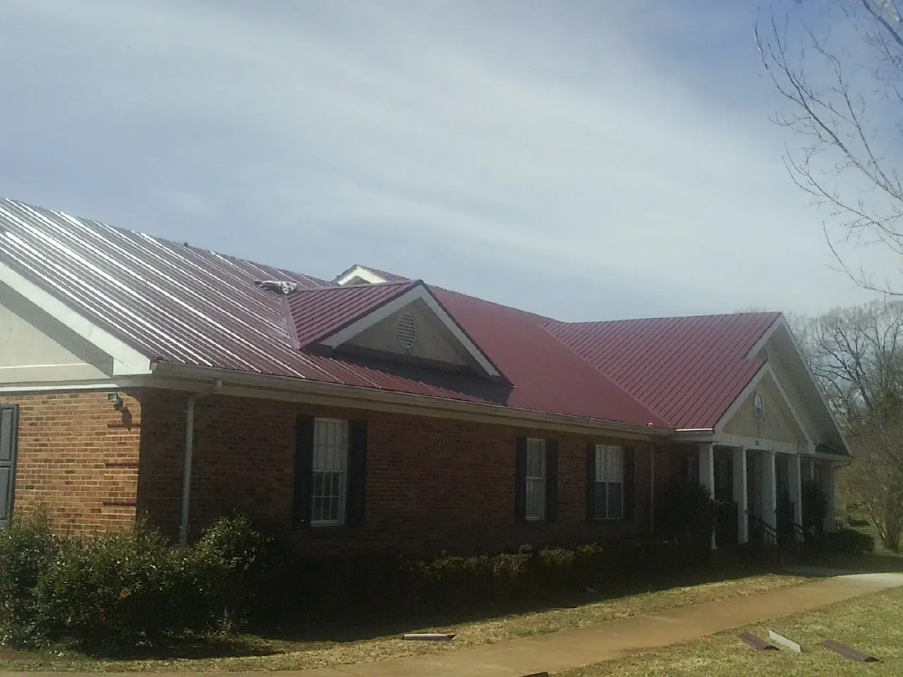 Red metal roof with gabled entries on a long brick building, from a Hail Damage Roof Repair job in Corvallis