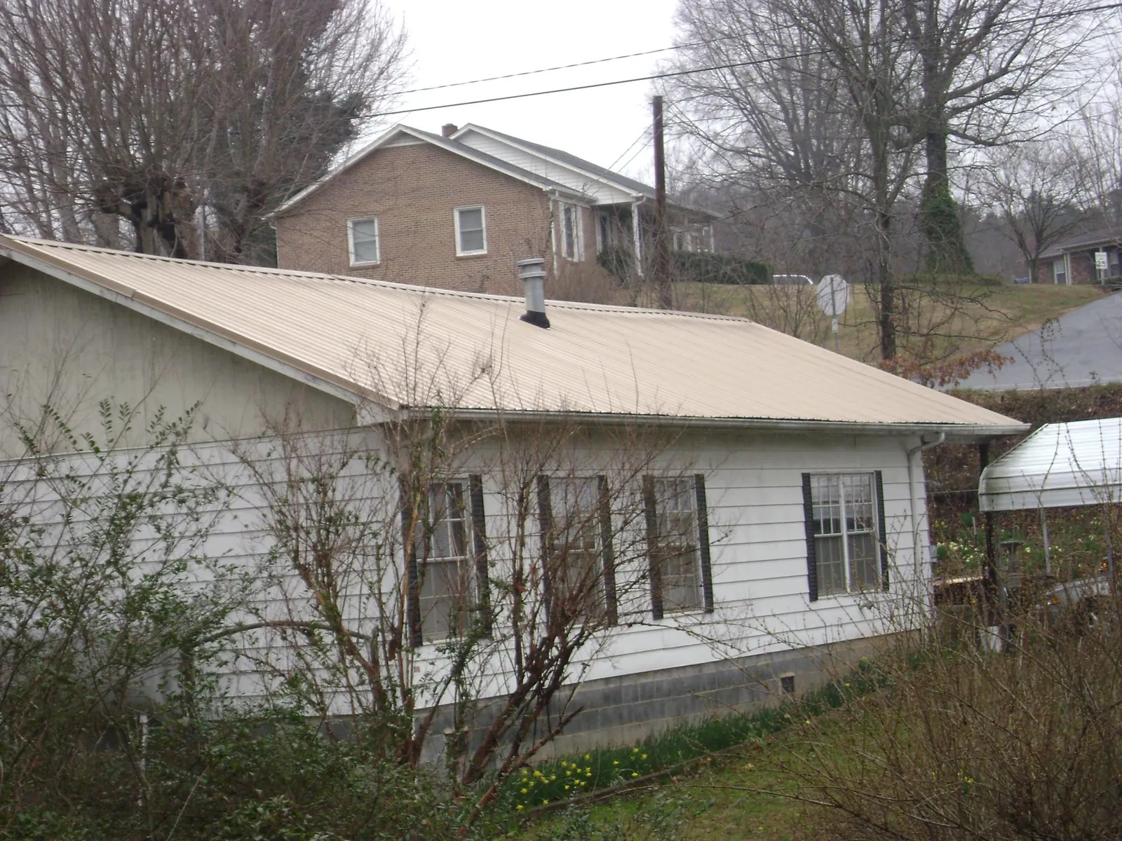 Tan metal roof on a white sided house set into a hillside — Commercial Roofing by Roofing Brothers in Corvallis